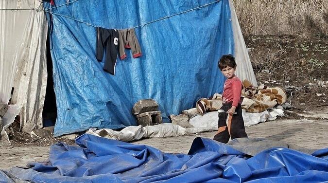 Pojke utan för sitt hem byggt av presenning vid syriska gränsen. 