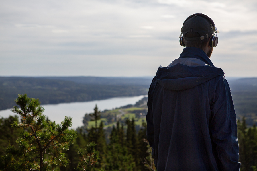 Foto: Maja Daniels En man med hörlurar syns bakifrån. Bakom honom syns en utsikt över sjö och landskap, från Hoverberget i södra Jämtland.