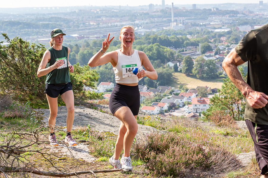 Foto: Göteborg Trail Run Tre personer springer i naturen, med utsikt över centrala Göteborg i bakgrunden. En kvinna ler stort in i kameran.