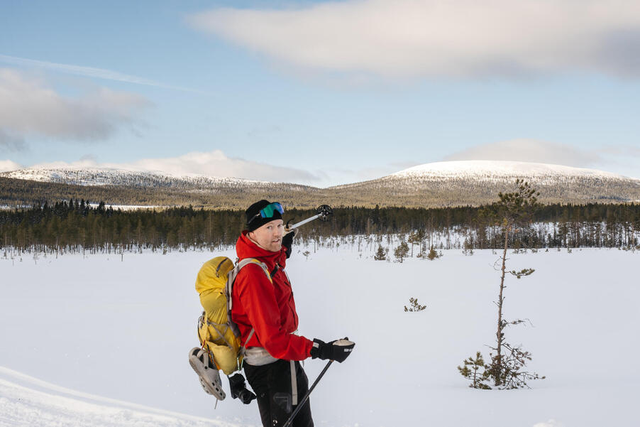 Foto på Oskar Karlin som pekar med en skidstav mot ett snöbeklätt berg.