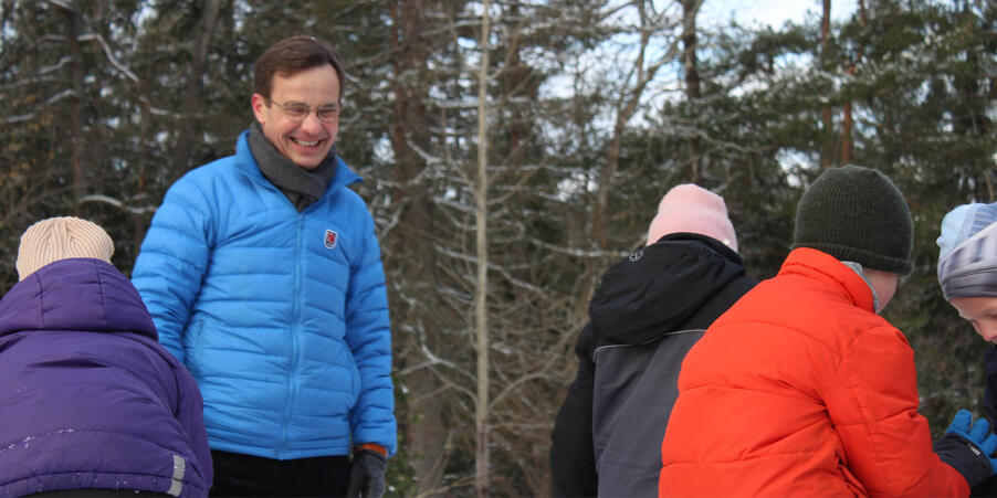Statsminister Ulf Kristersson i en blå jacka, tillsammans med en grupp barn.