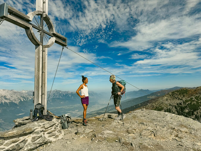 Foto: Anna W Thorbjörnsson Två personer står brevid ett kors på en bergstopp med utsikt över ett flertal andra bergstoppar.