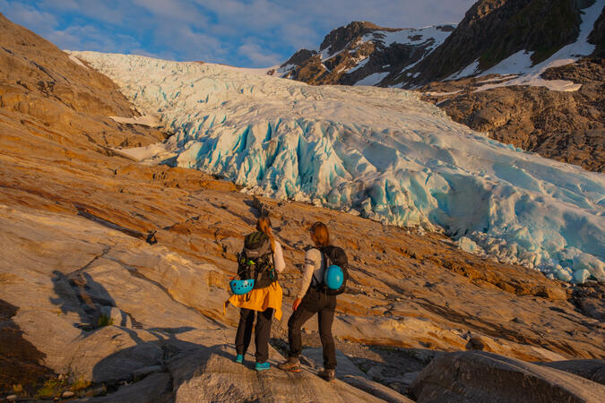 Engenbreen, Svartisen. Foto: Emilie Solbakken / Visit Helgeland Två personer står framför Engenbreen - där glaciären Svartisens möter havet.