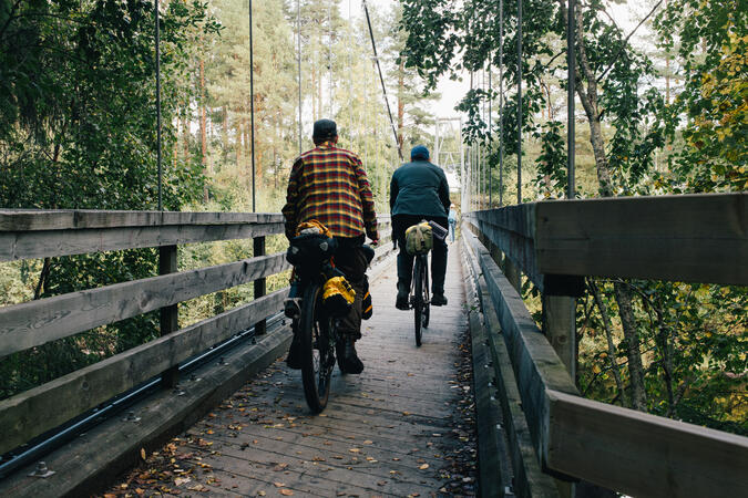 Två män cyklar på en träbro genom skog.