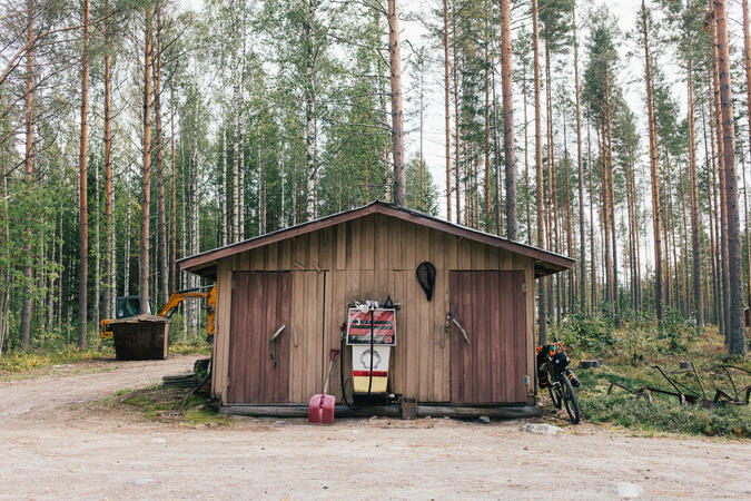 Ett hus i skogen längs en grusväg. Mot huset står en gravelbike lutad.