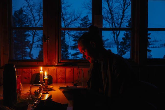 En person läser en bok framför tända ljus i en fjällstuga.