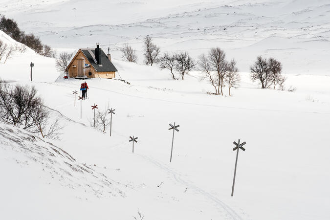 Två personer på skidor framför Gåsåns rastskydd i Jämtland.